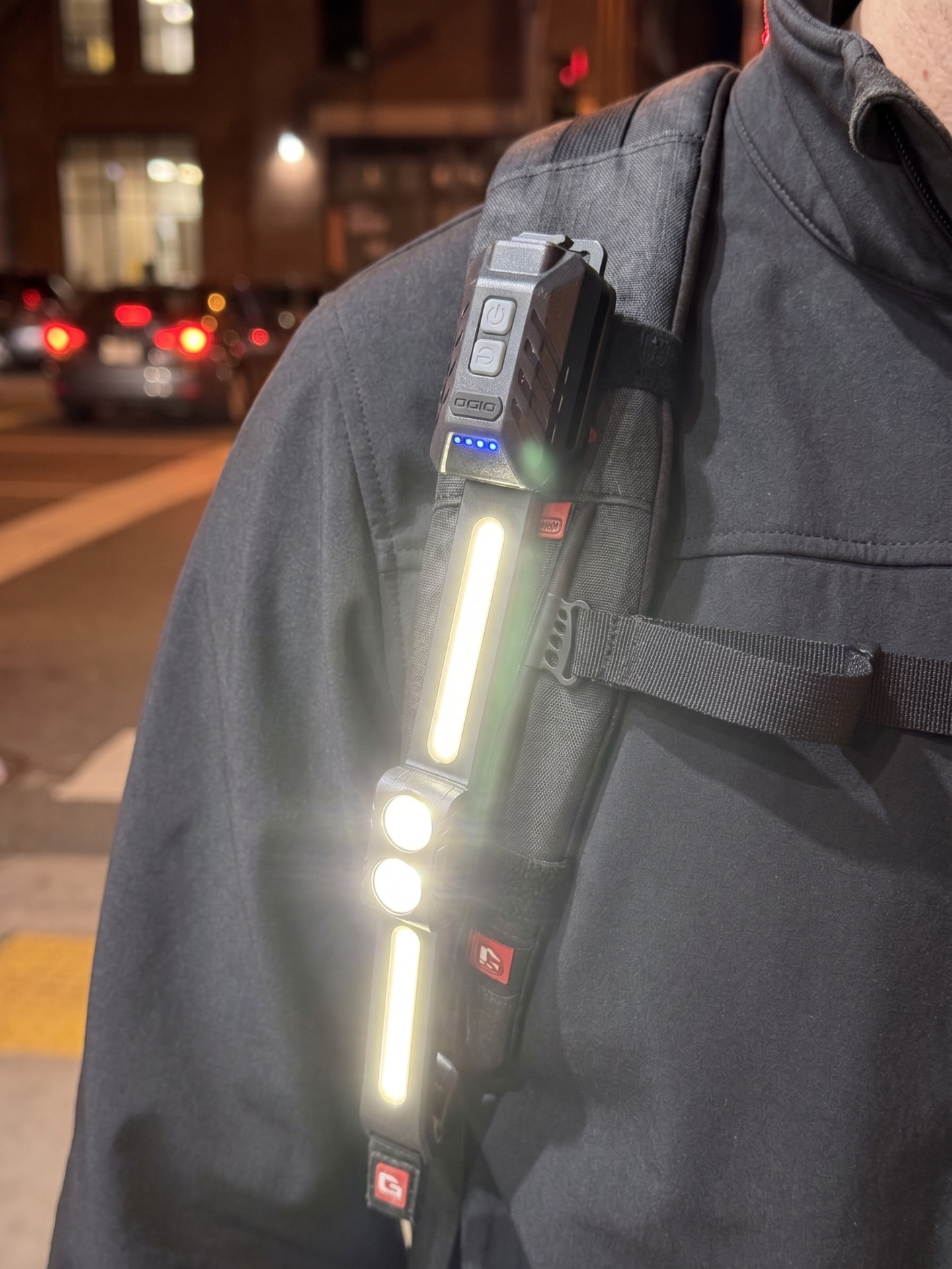 A person wearing two lit Straplights® units on their shoulder straps after dark